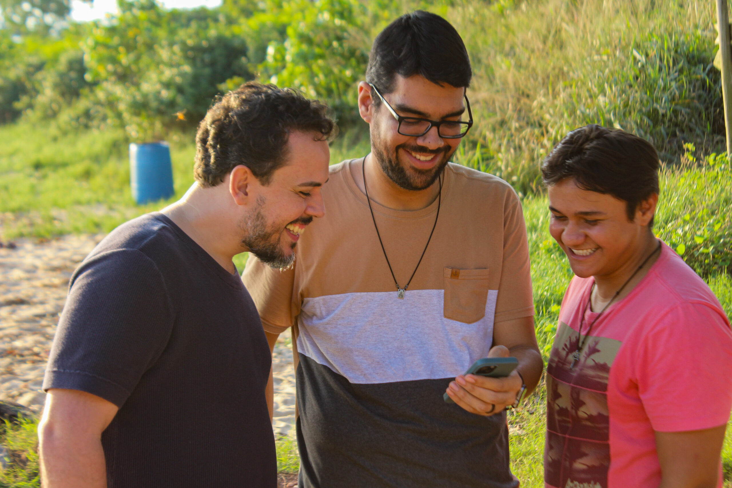 Três jovens conversam e leem juntos ao ar livre.