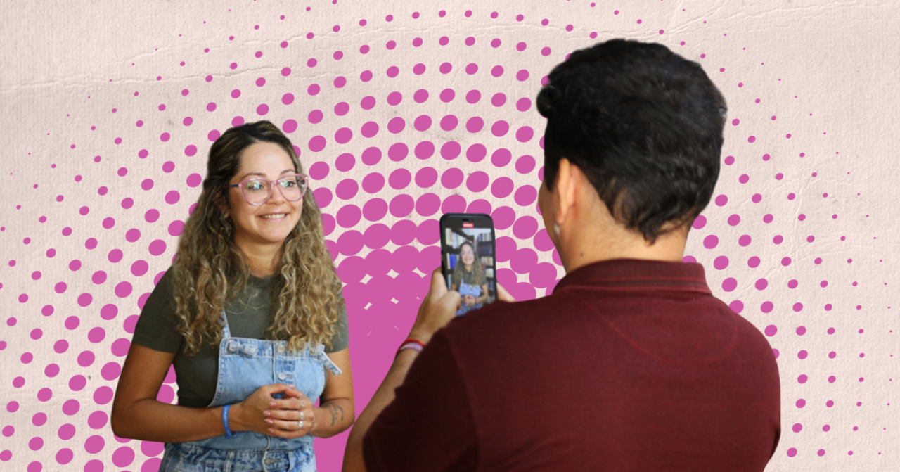 Duas pessoas participam de uma gravação em vídeo. Uma jovem aparece sorrindo enquanto é filmada por outra pessoa usando um celular. A imagem tem fundo gráfico com padrão de pontos em tons de rosa e textura clara.