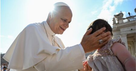 Papa Leão XIV, vestido de branco, abençoa uma criança durante encontro com fiéis na Praça São Pedro, no Vaticano.