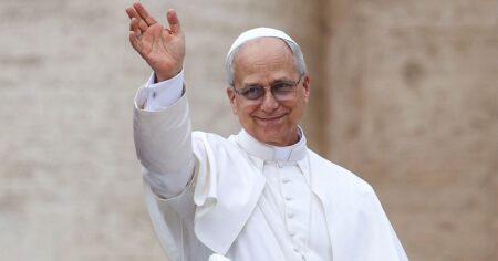 Papa Leão XIV, vestido de branco, sorri e acena com a mão direita durante aparição pública.