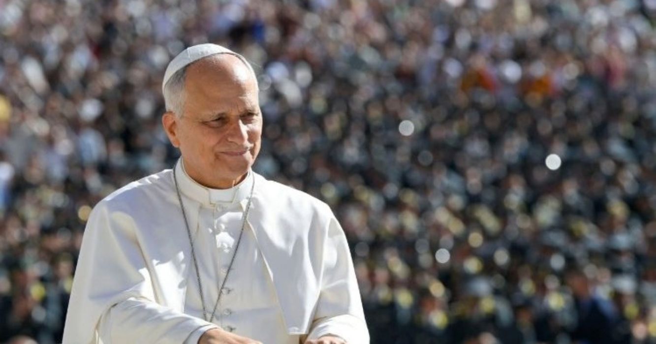 Papa Leão XIV, vestido de branco, caminha sorrindo diante de uma grande multidão reunida na Praça de São Pedro, no Vaticano.