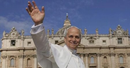 Papa Leão XIV acena sorrindo diante da Basílica de São Pedro, no Vaticano, sob céu azul.